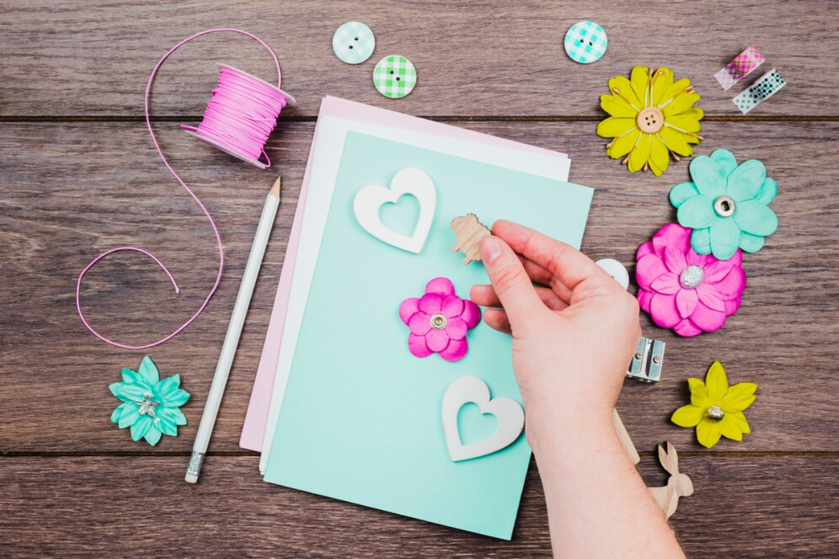 A hand places a wooden embellishment on colorful craft papers.
