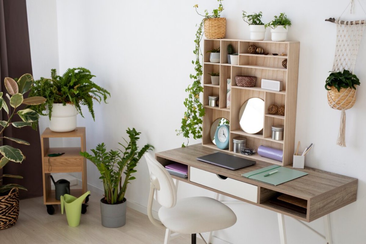 A well-organized desk with plants, a mirror, and decorative items against a light wall, creating a serene workspace ambiance.